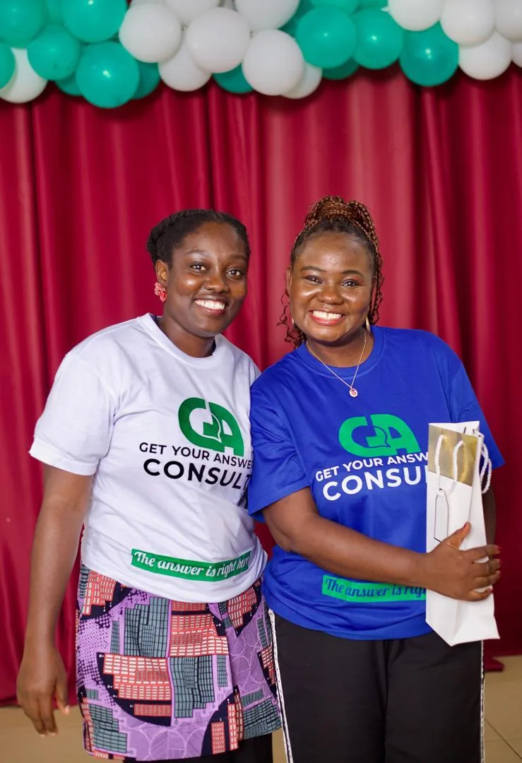 Two women wearing blue shirts and holding a gold bag.