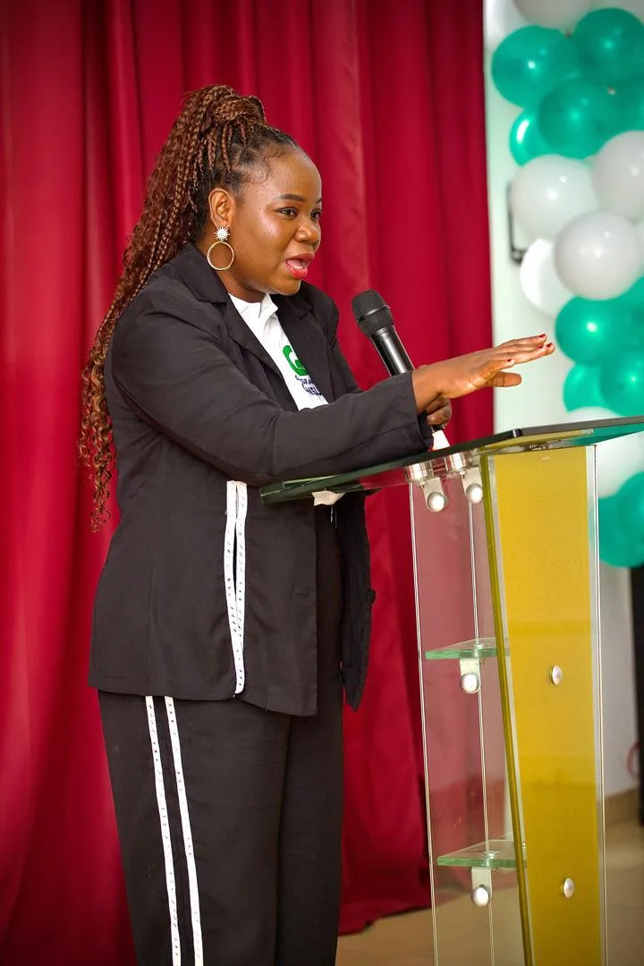 A woman in a black suit and white shirt speaks at a podium.
